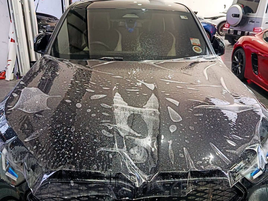 A BMW iX3 bonnet mid-installation, a sheet of paint protection film laid wet across it with slip solution beaded on the surface and the bonnet edges taped.
